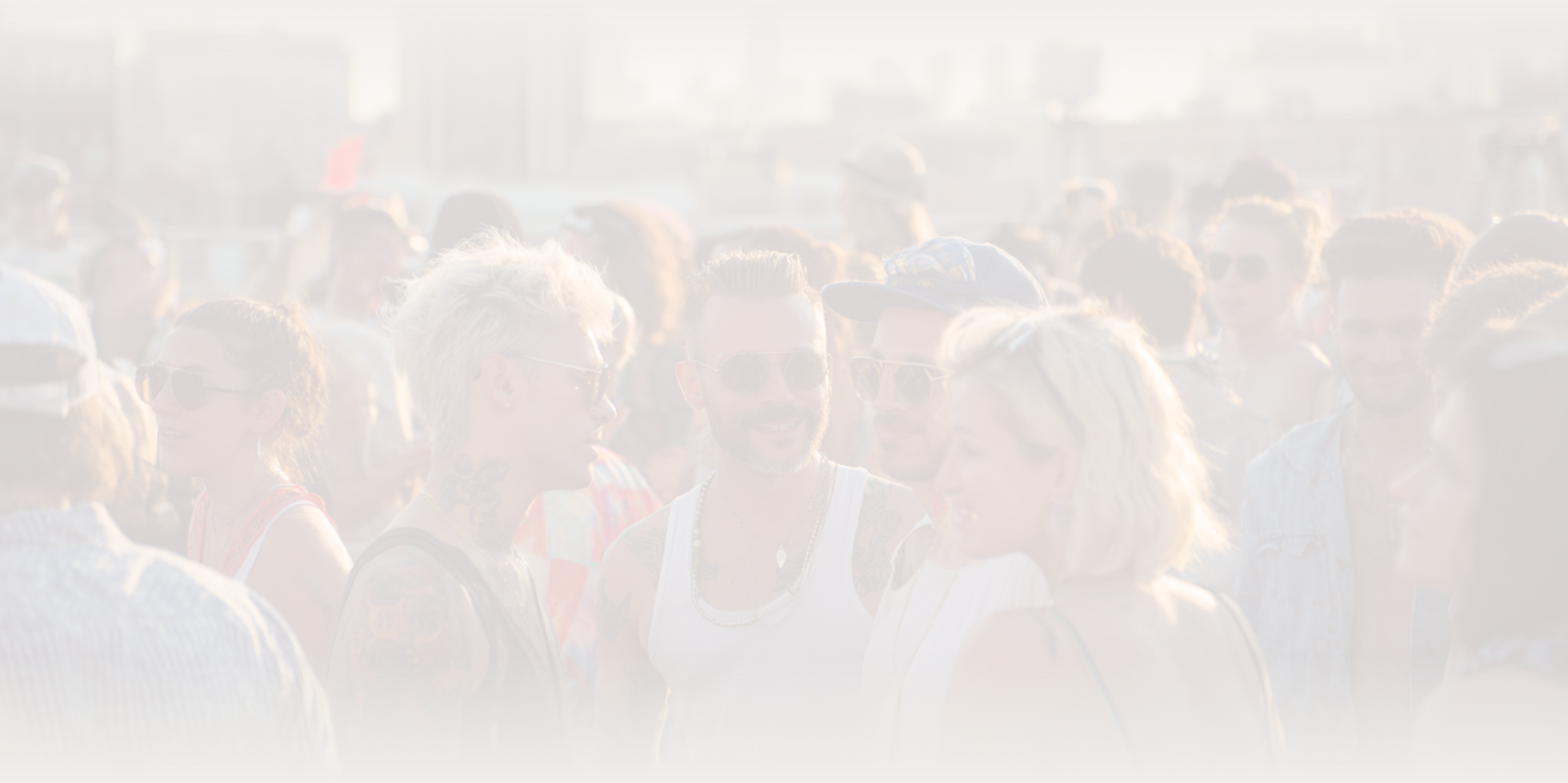 Group of young adults socializing at an outdoor event during sunset, many wearing sunglasses and casual summer clothes.