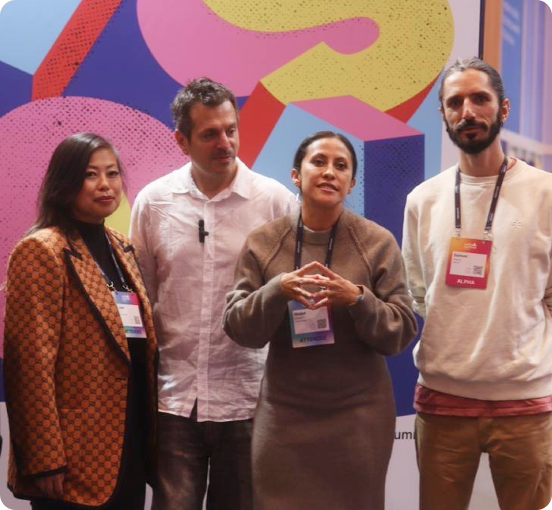 Four people standing in front of a colorful abstract mural at a conference, wearing event badges.