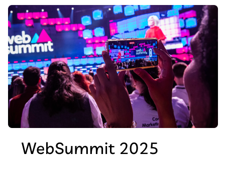 Audience member capturing a speaker on stage at the Web Summit 2025 event with colorful screens in the background.